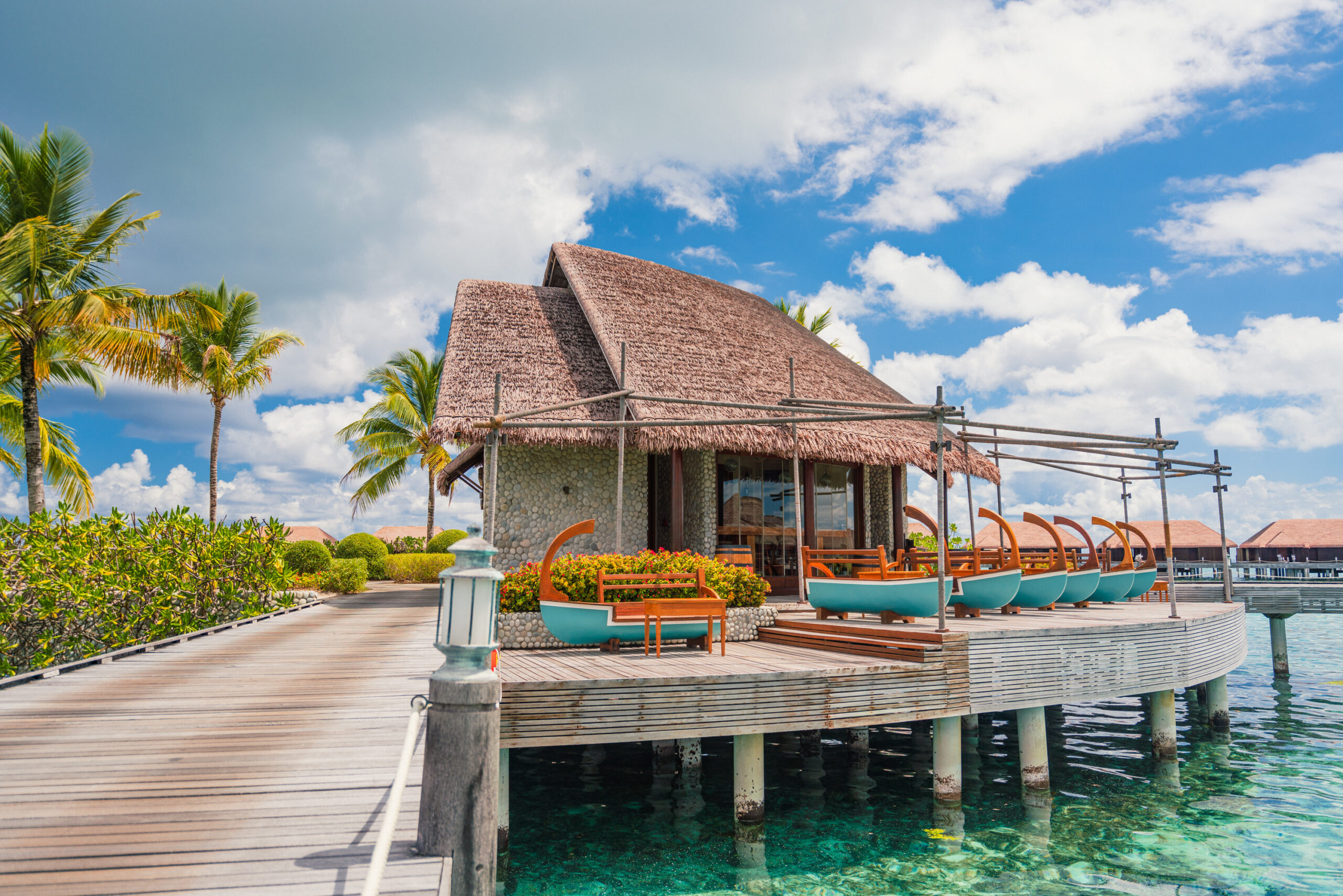 Overwater restaurant at Ayada Maldives with a thatched roof and ocean views on a sunny day