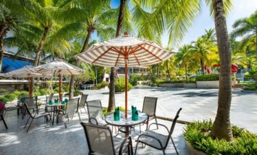 Patio dining at Chada Thai Village with umbrella-covered tables set among palm trees and tropical plants