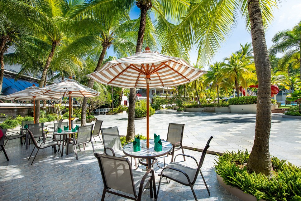 Patio dining at Chada Thai Village with umbrella-covered tables set among palm trees and tropical plants