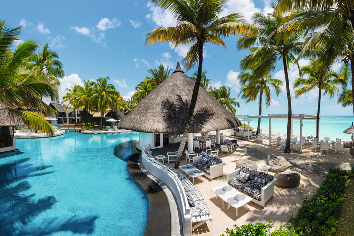 Pool area at Constance Belle Mare Plage with palm trees and thatched roof buildings by the water