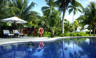Pool with reflections of palm trees and sun loungers at Paradise Sun