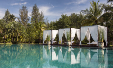 Poolside cabanas at The Sarojin Khao Lak with white drapes surrounded by lush greenery and palm trees