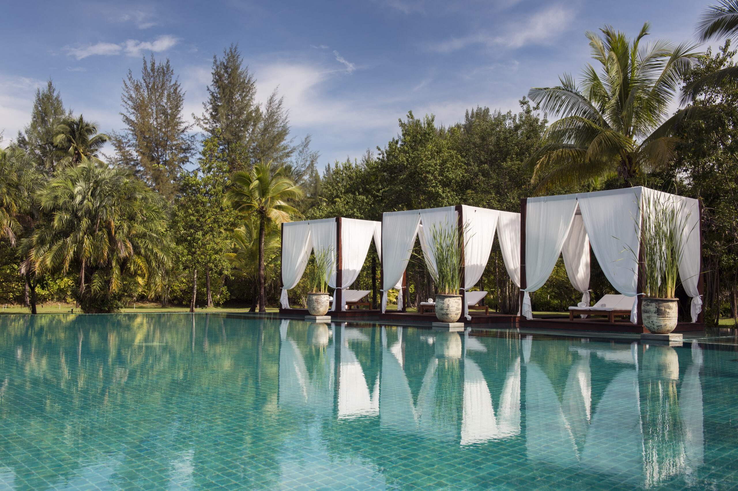 Poolside cabanas at The Sarojin Khao Lak with white drapes surrounded by lush greenery and palm trees