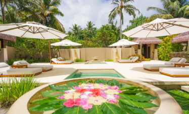 Relaxing pool area with lounge chairs and umbrellas at Ayada Maldives surrounded by tropical vegetation
