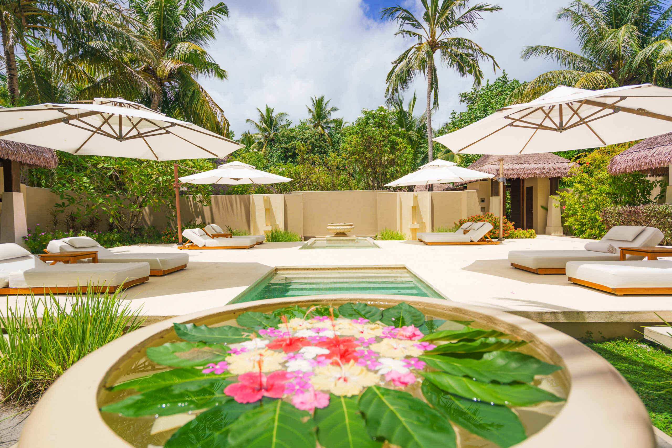 Relaxing pool area with lounge chairs and umbrellas at Ayada Maldives surrounded by tropical vegetation