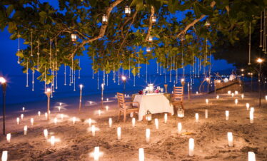 Romantic beach dinner setup with candlelit pathways under a tree at The Sarojin Khao Lak