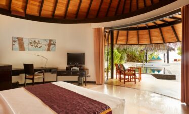 Sun Siyam Iru Fushi beachfront villa interior with a view of the private pool and beach beyond from the bedroom