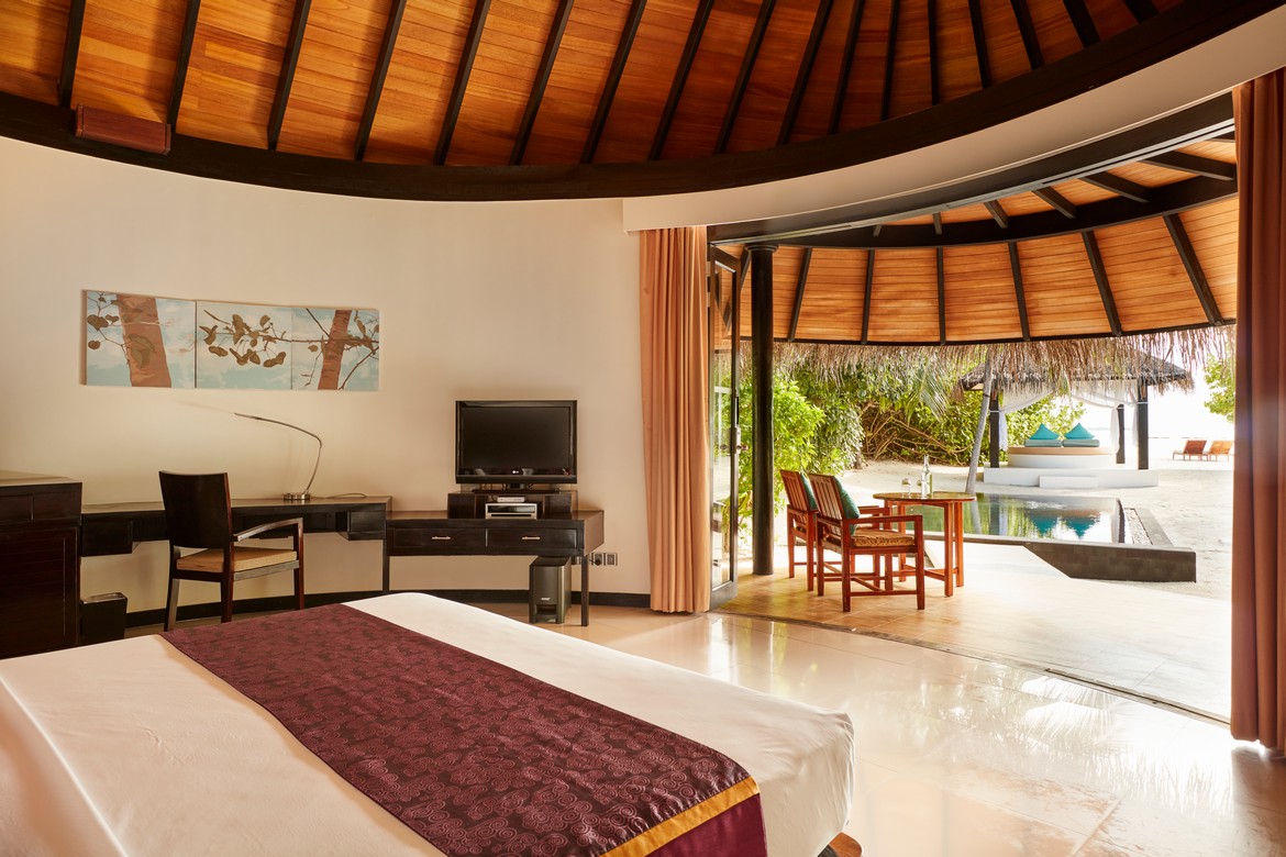 Sun Siyam Iru Fushi beachfront villa interior with a view of the private pool and beach beyond from the bedroom