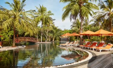 Sun Siyam Iru Fushi tropical pool area surrounded by palm trees and orange lounge chairs under the bright sun