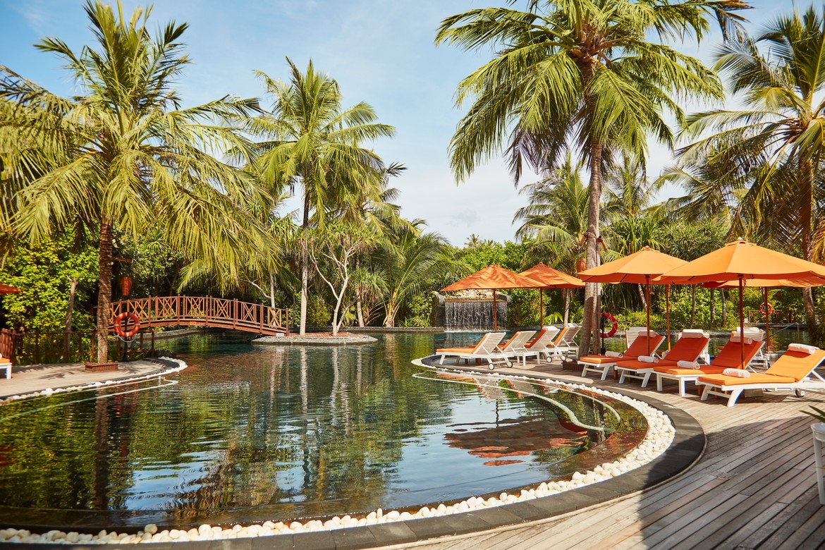 Sun Siyam Iru Fushi tropical pool area surrounded by palm trees and orange lounge chairs under the bright sun
