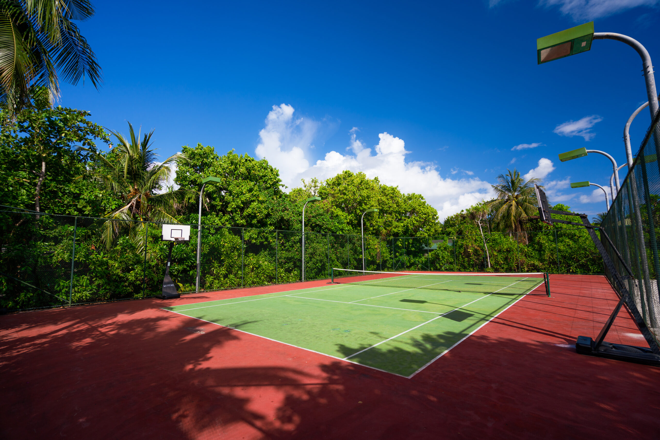 Tennis court surrounded by lush tropical greenery at Ayada Maldives under a bright blue sky
