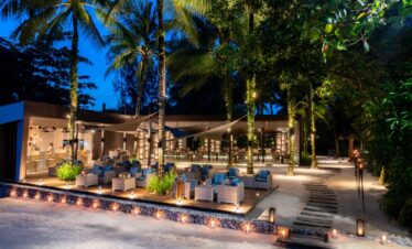 The Sarojin Khao Lak beachfront bar and lounge area illuminated at night with palm trees and seating