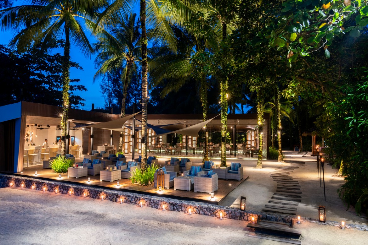 The Sarojin Khao Lak beachfront bar and lounge area illuminated at night with palm trees and seating