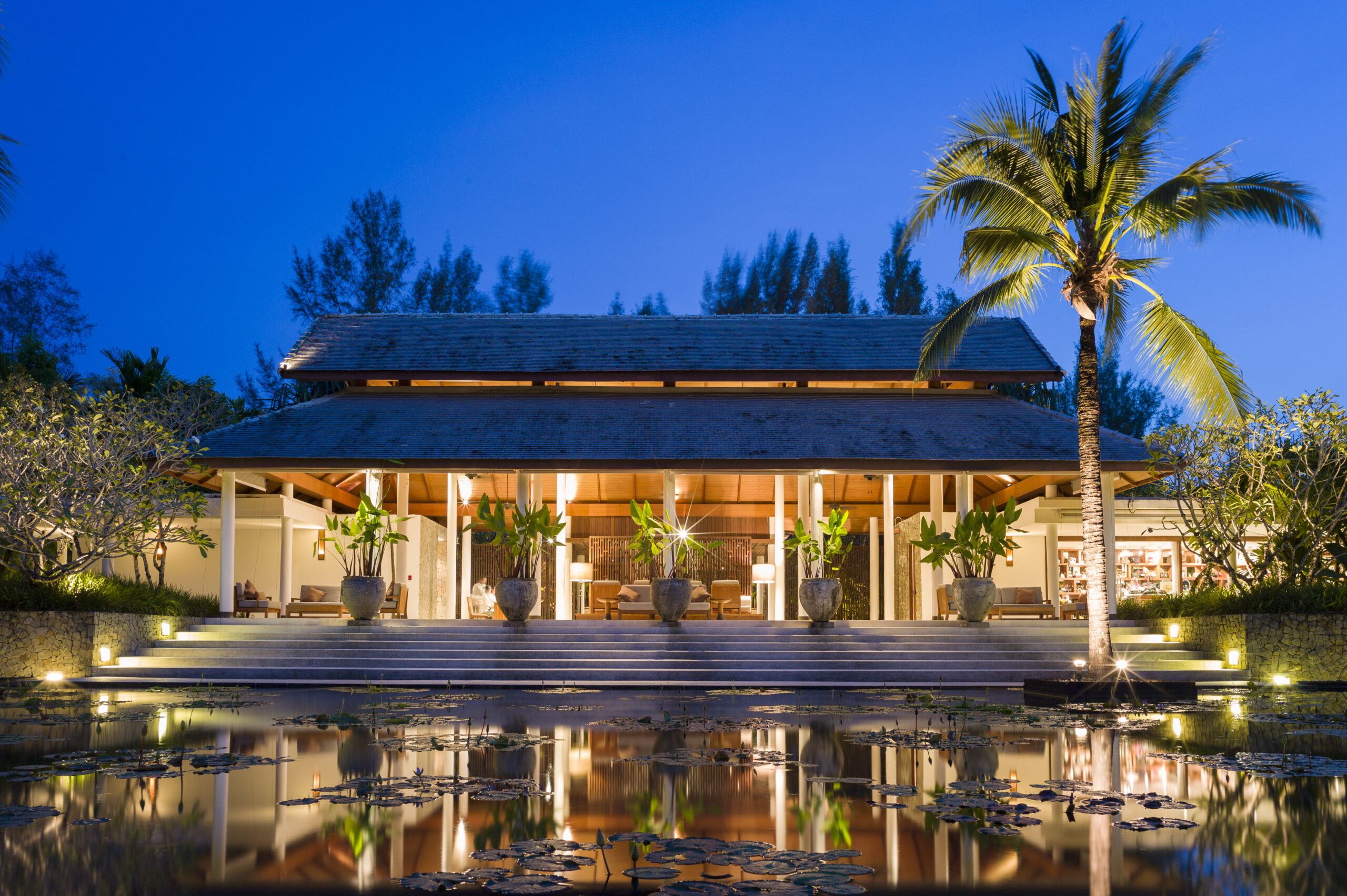 The Sarojin Khao Lak resort lobby at night with reflecting pond and tropical plants in front