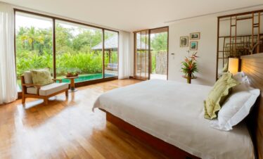 The Sarojin Khao Lak villa bedroom with floor to ceiling windows overlooking a private garden and pool