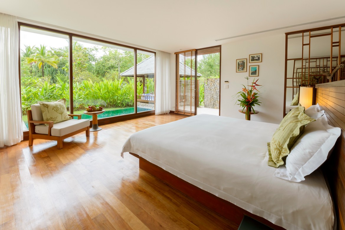 The Sarojin Khao Lak villa bedroom with floor to ceiling windows overlooking a private garden and pool