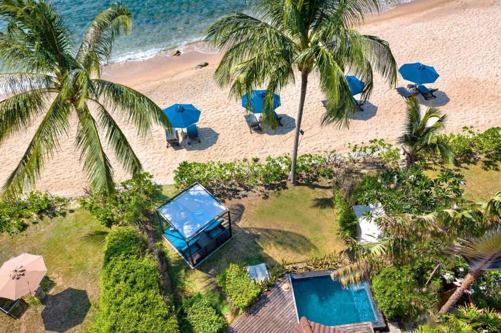 Aerial view of the beachfront at Saii Koh Samui with blue umbrellas and palm trees