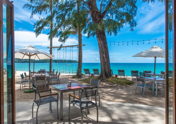 Beachfront dining setup at Saii Laguna under umbrellas with swings and sea view