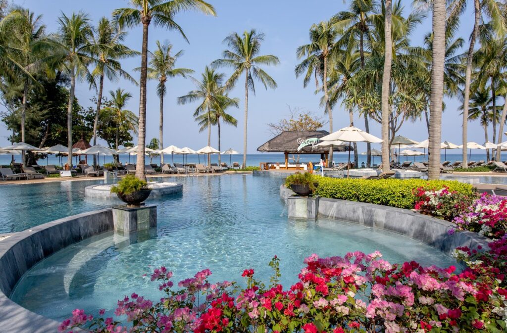 Katathani pool area surrounded by palm trees and vibrant flowers near the sea