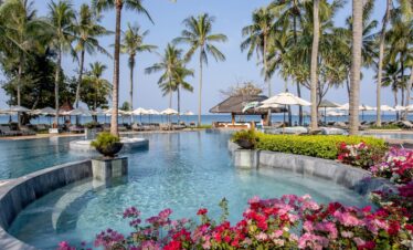 Katathani pool area surrounded by palm trees and vibrant flowers near the sea