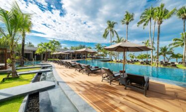 Relaxing pool area with sun loungers under palm trees at La Flora Khao Lak