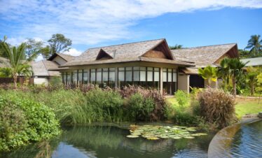 A serene resort villa with large windows and a pond surrounded by lush plants Story of peaceful retreat