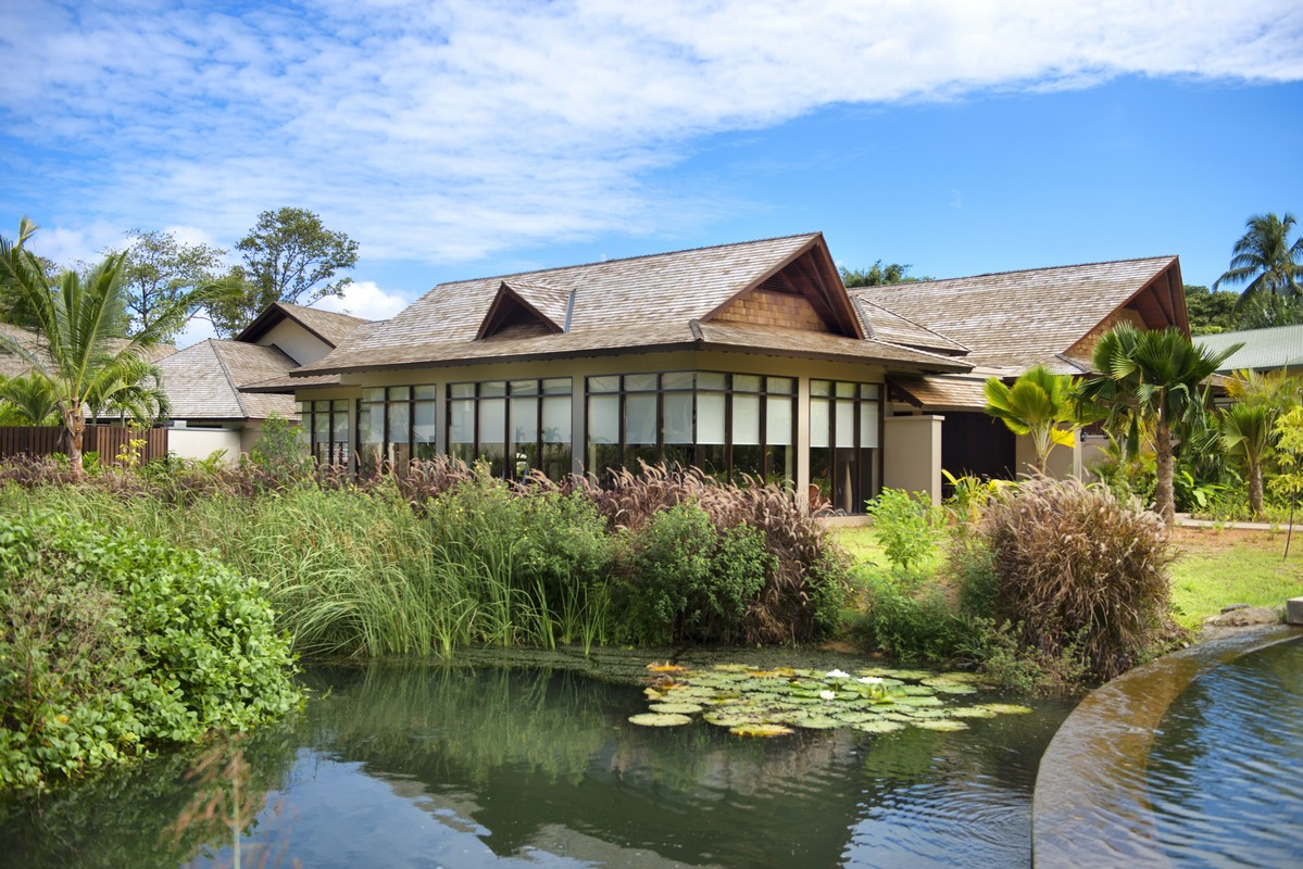 A serene resort villa with large windows and a pond surrounded by lush plants Story of peaceful retreat