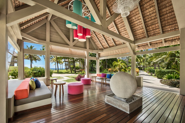 Open-air lounge at Solana Beach with colorful seating and garden view under a thatched roof