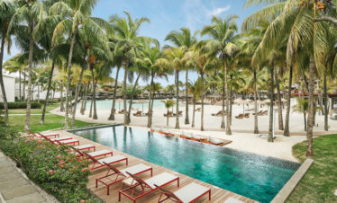 Poolside relaxation area with palm trees and sun loungers at Paradise Cove Boutique