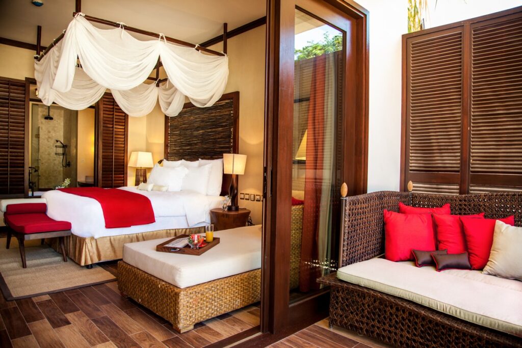 Story of a cozy resort bedroom with a canopy bed and vibrant red accents connected to an outdoor seating area
