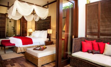 Story of a cozy resort bedroom with a canopy bed and vibrant red accents connected to an outdoor seating area