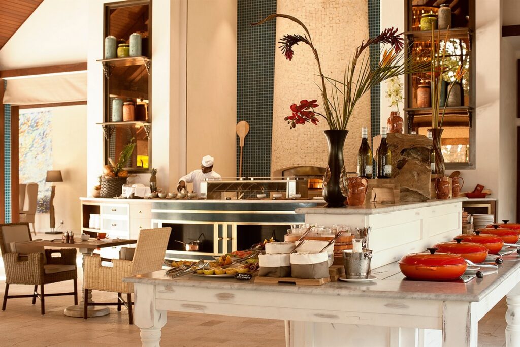 Story of a dining area in a resort with a chef preparing food and elegant table settings with tropical decor