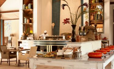 Story of a dining area in a resort with a chef preparing food and elegant table settings with tropical decor