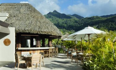 Story of an outdoor dining area at a resort with thatched roofs and mountain views surrounded by greenery
