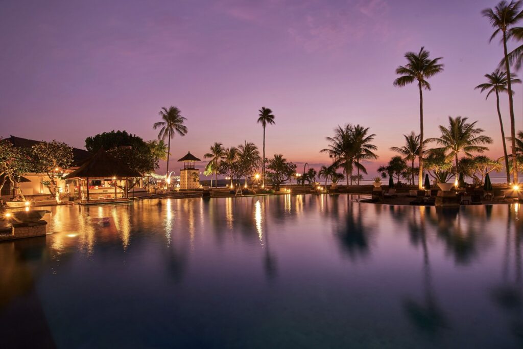 Sunset over the pool at Patra Bali Resort and Villas with palm trees