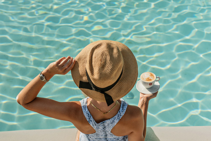Woman with sun hat enjoying a poolside coffee at Nirvana At Le Meridien Ilse Mauritius under the sun