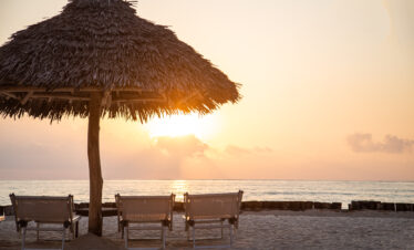 Beachfront with straw umbrellas and sun loungers at Tui Blue Bahari overlooking a sunset