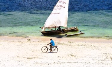 Dream of Zanzibar beachfront with dhow and cyclist