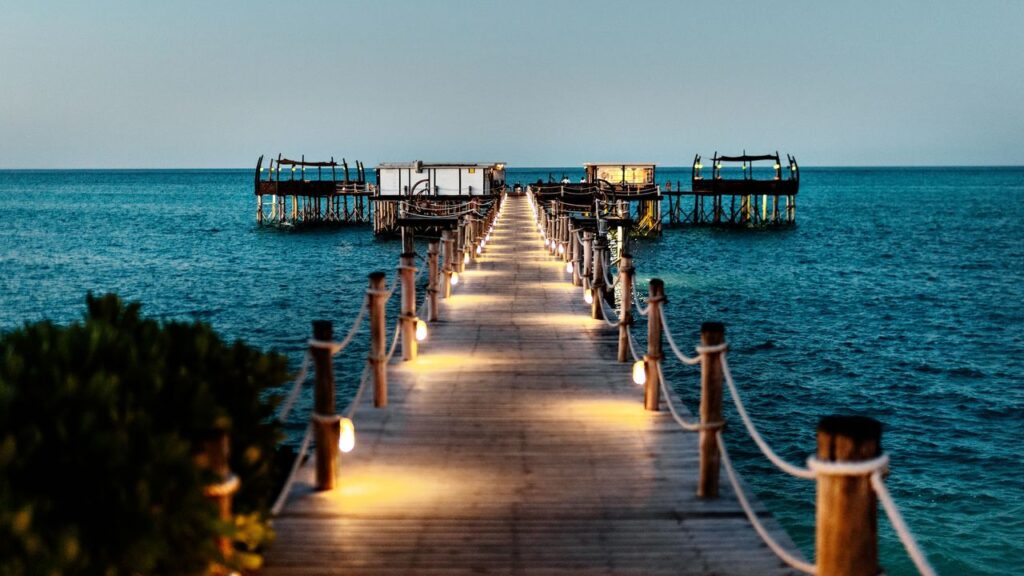 Illuminated wooden jetty at Essque Zalu Zanzibar leading to overwater bungalows