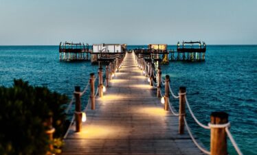 Illuminated wooden jetty at Essque Zalu Zanzibar leading to overwater bungalows