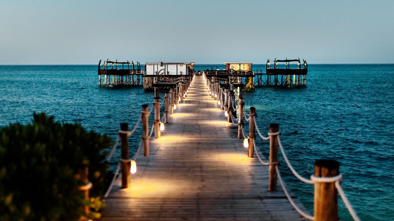 Illuminated wooden jetty at Essque Zalu Zanzibar leading to overwater bungalows